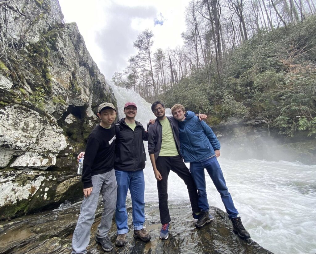 Four students stand in front of a waterfall on a WUD Alternative Breaks trip to Walland, Tennessee.