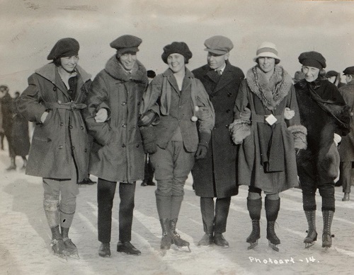 A group of five men and women pose on the ice, while bedecked in winter layers and ice skates 