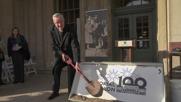 mark guthier holds shovel in front of memorial union 100 sign at memorial union